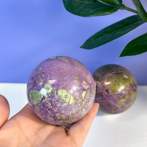 Hand holding an imperfect stichtite sphere with vibrant purple and green marbling.