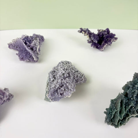 Assorted grape agate clusters featuring bumpy, crystalline purple and teal textures on a white surface.