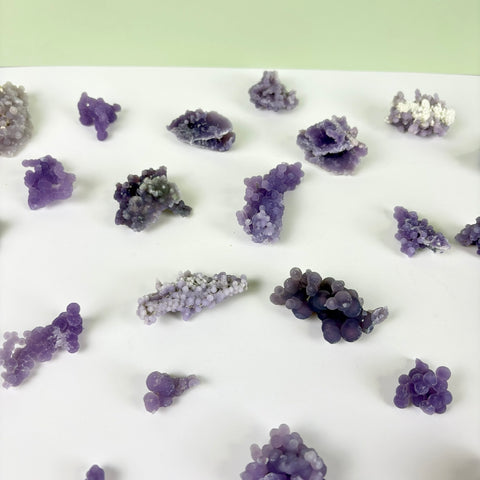 Small, bubbly purple grape agate crystal clusters arranged on a white surface.
