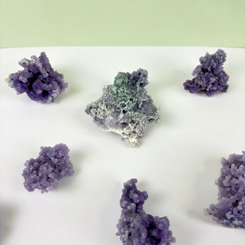 Clusters of purple grape agate crystals with bumpy, botryoidal textures arranged on a white surface.