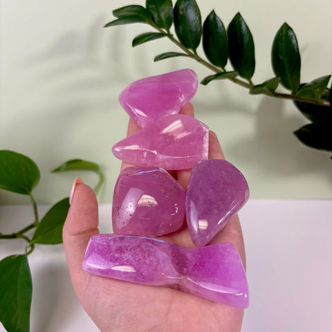 Hand holding four polished, translucent jelly pink aragonite free form crystals with smooth, rounded edges.