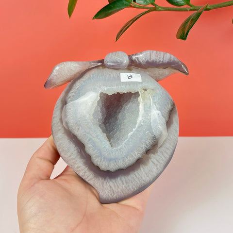 Peach-shaped agate carving with a sparkling druzy geode center, held in a hand against a coral background.