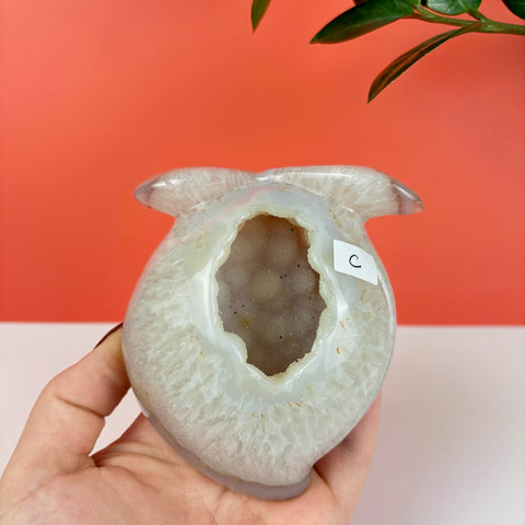 Peach-shaped druzy agate crystal with a sparkling hollow center held in a hand against a coral background.