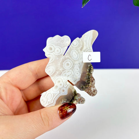 Handheld kneeling fairy princess carving made of scenic moss agate with white circular patterns and earthy inclusions.