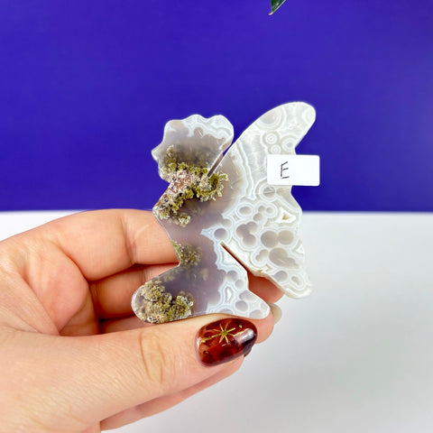 Handheld kneeling fairy carving made of scenic moss agate with intricate white banding and green mossy inclusions.