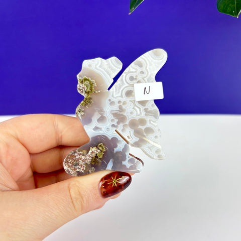 Handheld kneeling fairy princess carving made of translucent scenic moss agate with intricate white patterns.