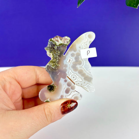 Handheld kneeling fairy figurine carved from scenic moss agate with intricate white and grey banded patterns.