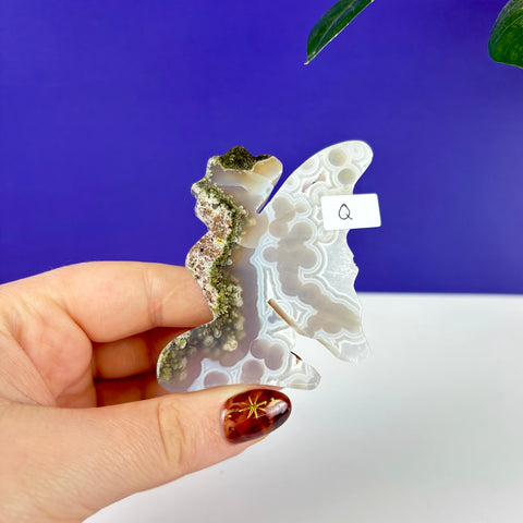 Handheld kneeling fairy carving made of translucent moss agate with green mineral inclusions and white banding.