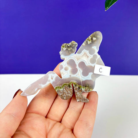 Handheld lounging fairy carving made of translucent moss agate with green mineral inclusions and banded patterns.