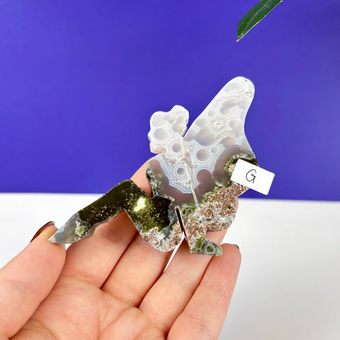 Handheld lounging fairy princess carving made of scenic moss agate with white druzy circles and green mossy inclusions.