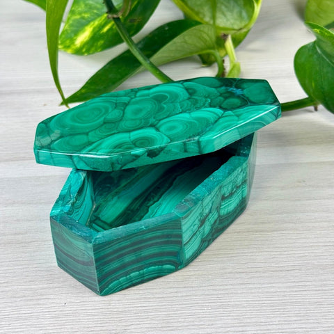 Hexagonal malachite jewellery box with vibrant green swirling patterns and a polished stone lid on a wooden surface.