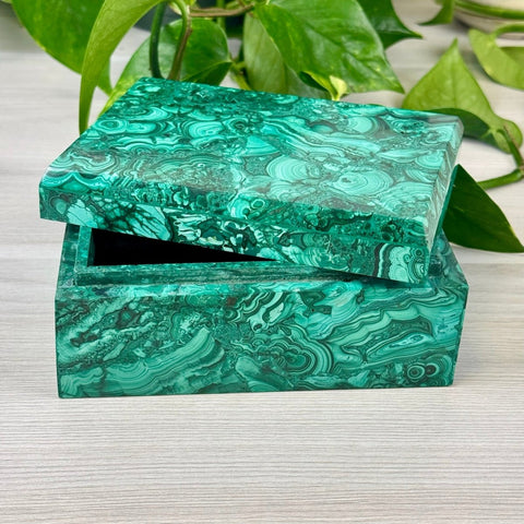 Rectangular malachite jewellery box with vibrant green swirling patterns and a partially open lid on a light wooden surface.