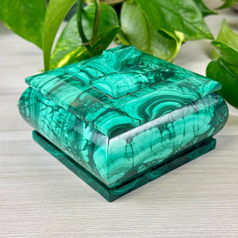 Square malachite jewellery box with a vibrant green banded pattern and a stepped lid design on a light wooden surface.