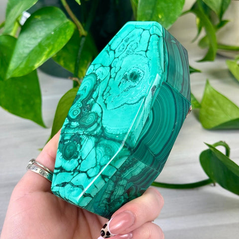 Handheld polished malachite jewellery box featuring vibrant green banded patterns and a unique geometric coffin shape.