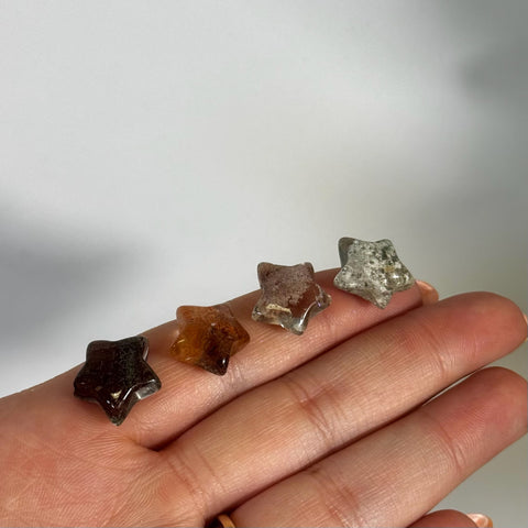 Four mini garden quartz star crystals in varying shades of brown, orange, and clear, held in a hand.