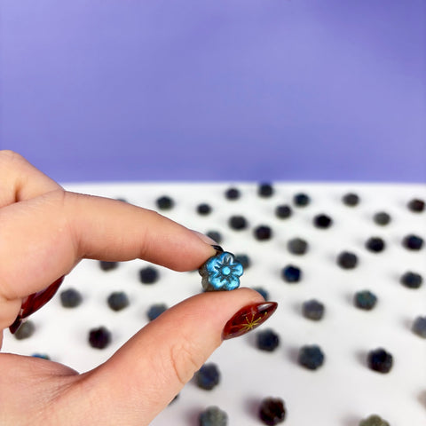 Hand holding a small, carved labradorite daisy with iridescent blue flashes against a white and purple background.