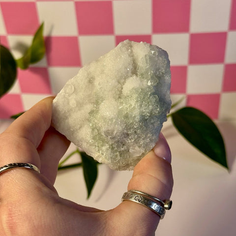 Hand holding a mint-green fluorite with calcite specimen against a pink checkered background.