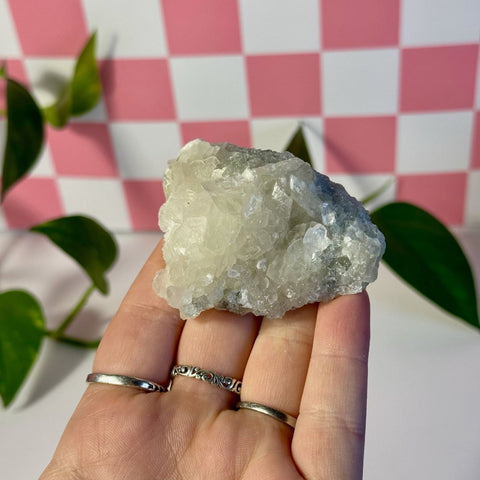 Hand holding a mint-green fluorite with calcite specimen against a pink and white checkered background.