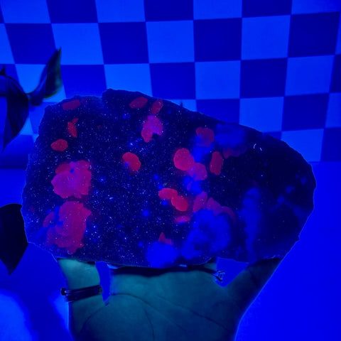 Mint-green fluorite with calcite specimen glowing bright red and blue under UV light, held in a hand.