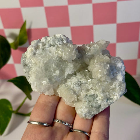 Mint-green fluorite with calcite specimen held in hand, against a pink and white checkered background.