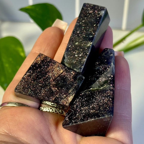 Three dark purple Mystery Galaxy Iolite crystal towers with sparkling pink and gold flecks in a hand.