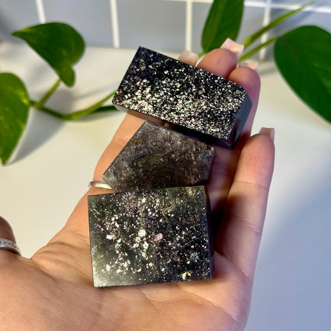 Three rectangular Mystery Galaxy Iolite crystals, dark with sparkling inclusions, held in a hand.