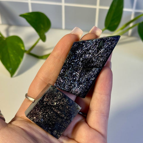 Two polished Mystery Galaxy Iolite stones, one rectangular and one trapezoidal, held in a hand.