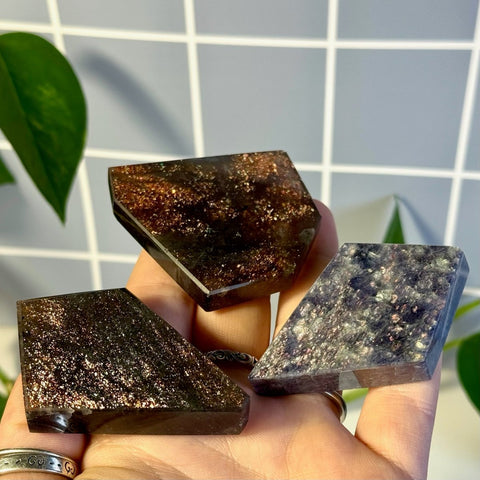 Three faceted, dark brown and purple Mystery Galaxy Iolite crystals with sparkling inclusions held in a hand.