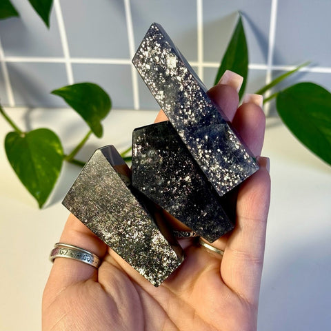 Hand holding three dark, sparkly Mystery Galaxy Iolite crystal towers with faceted sides.