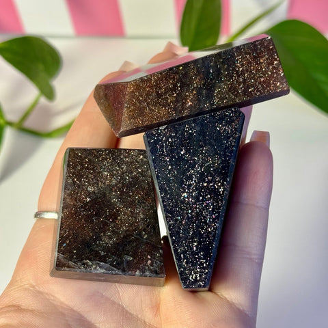 Three dark, glittery Mystery Galaxy Iolite crystals in various geometric shapes held in a hand.