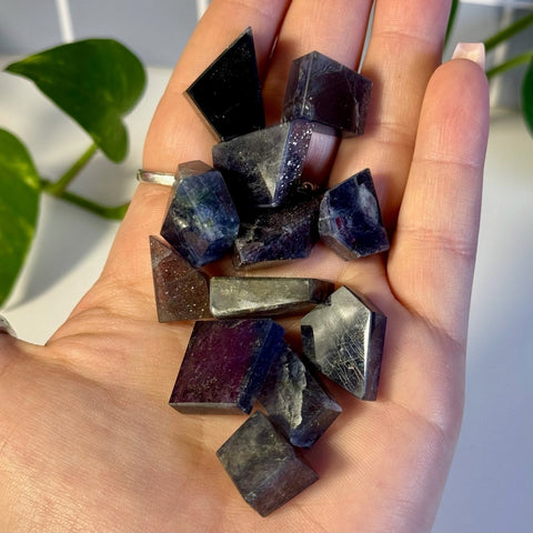 Hand holding multiple dark purple, faceted Mystery Galaxy Iolite crystal pieces.