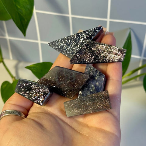 Hand holding several dark, sparkly Mystery Galaxy Iolite crystal shards.