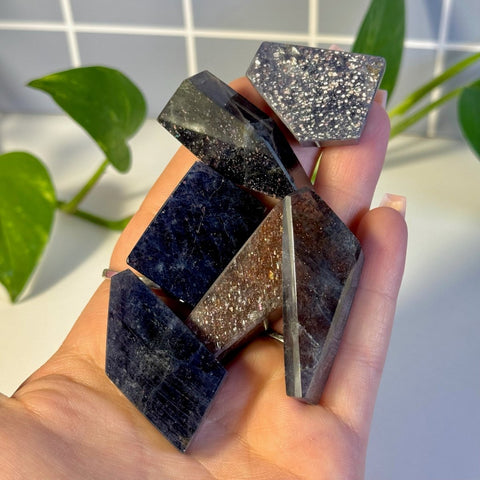 Hand holding various faceted Mystery Galaxy Iolite crystals in dark blue, brown, and sparkling silver.