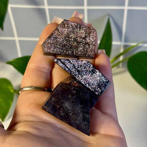 Shimmering Mystery Galaxy Iolite crystals in various geometric cuts, held in a hand.