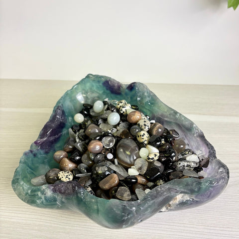 Hand-carved fluorite bowl filled with a variety of polished black, white, and brown gemstone crystals.