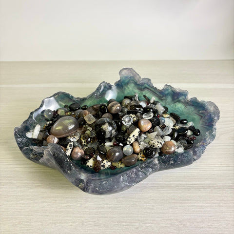 Rough-edged fluorite bowl filled with a variety of polished black, white, and brown gemstone pebbles and spheres.