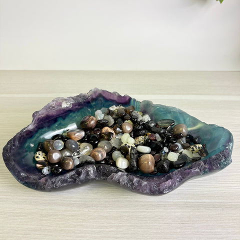 Polished fluorite bowl with purple and teal hues filled with a variety of smooth, multi-colored gemstone crystals.
