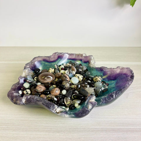 Hand-carved fluorite bowl featuring purple and green hues filled with a variety of polished gemstone crystals.