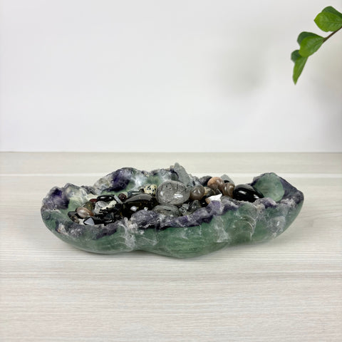 Hand-carved fluorite crystal bowl in green and purple hues filled with assorted polished gemstone tumble stones.