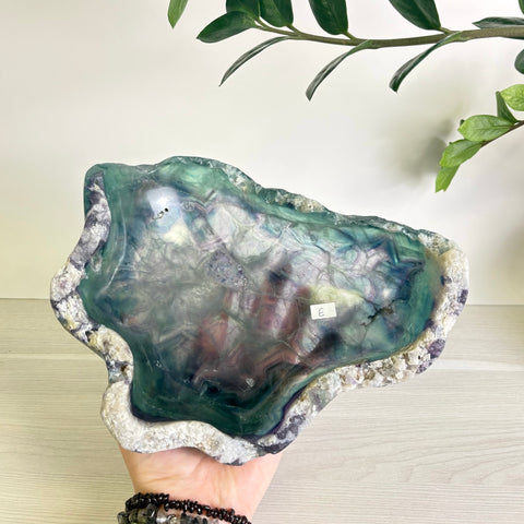 Hand-carved fluorite bowl featuring translucent green and purple mineral patterns with a natural, rough-hewn stone edge.