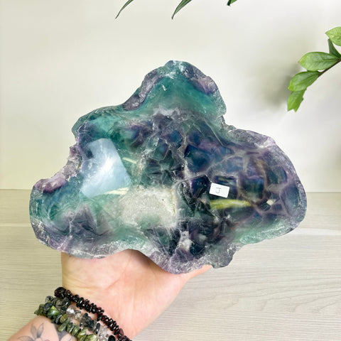 Handheld fluorite bowl featuring vibrant swirls of deep purple, teal, and green with a polished, organic crystal texture.