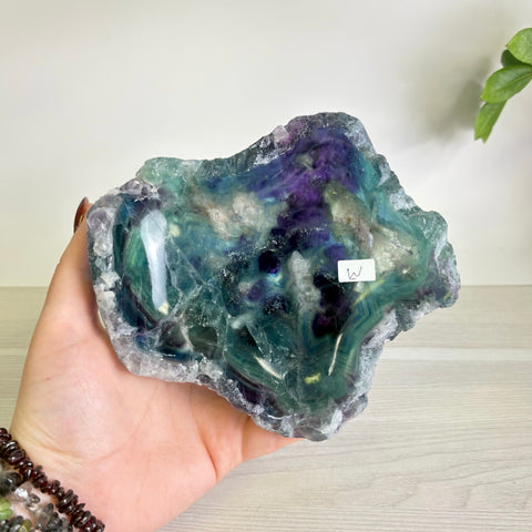 Handheld polished fluorite bowl featuring vibrant swirls of deep purple, teal, and green with a natural raw crystal edge.