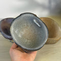 Hand holding a natural gray and white agate bowl with polished interior. Two other agate bowls visible in background.