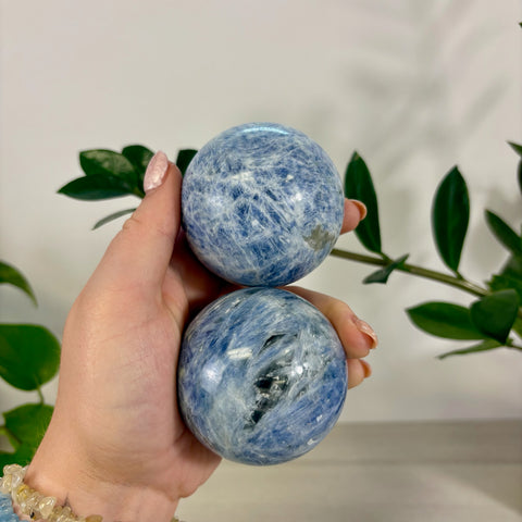 Hand holding two polished ocean blue kyanite spheres with natural white veining and crystalline textures.
