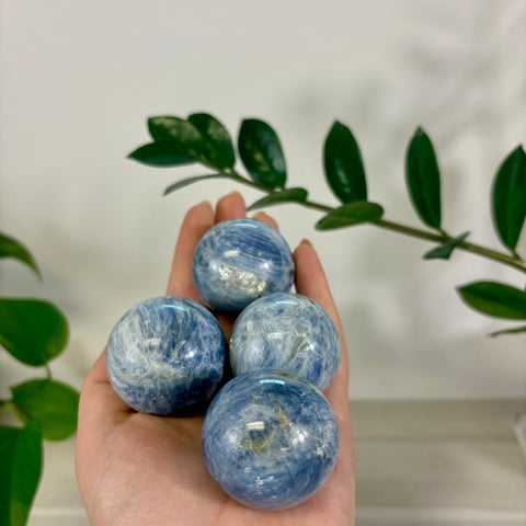 Hand holding four polished ocean blue kyanite spheres with natural white mineral inclusions and a smooth, glossy finish.