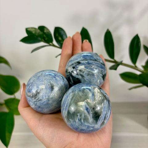 Three polished ocean blue kyanite spheres with marbled blue and grey patterns held in a palm.