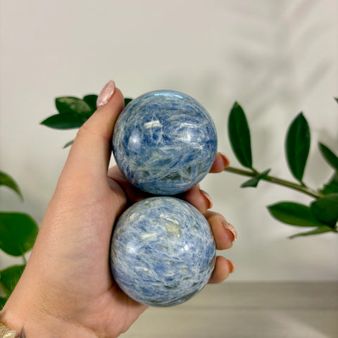 Hand holding two polished ocean blue kyanite spheres with natural crystalline patterns and glossy finishes.