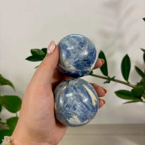 Hand holding two polished ocean blue kyanite spheres with natural white veining and crystalline textures.