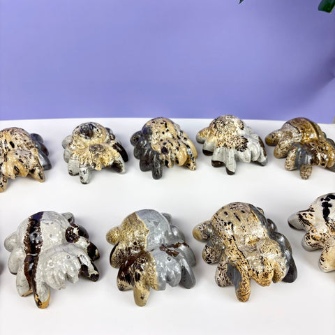 Hand-painted stone spider figurines with speckled, metallic, and natural stone patterns arranged on a white surface.