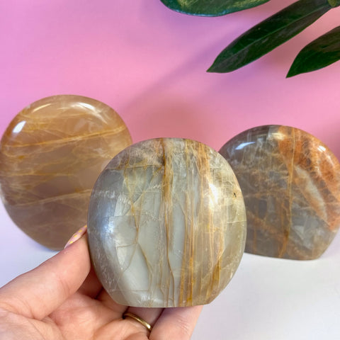 Hand holding a smooth, polished peach moonstone free form with subtle orange and gray tones.
